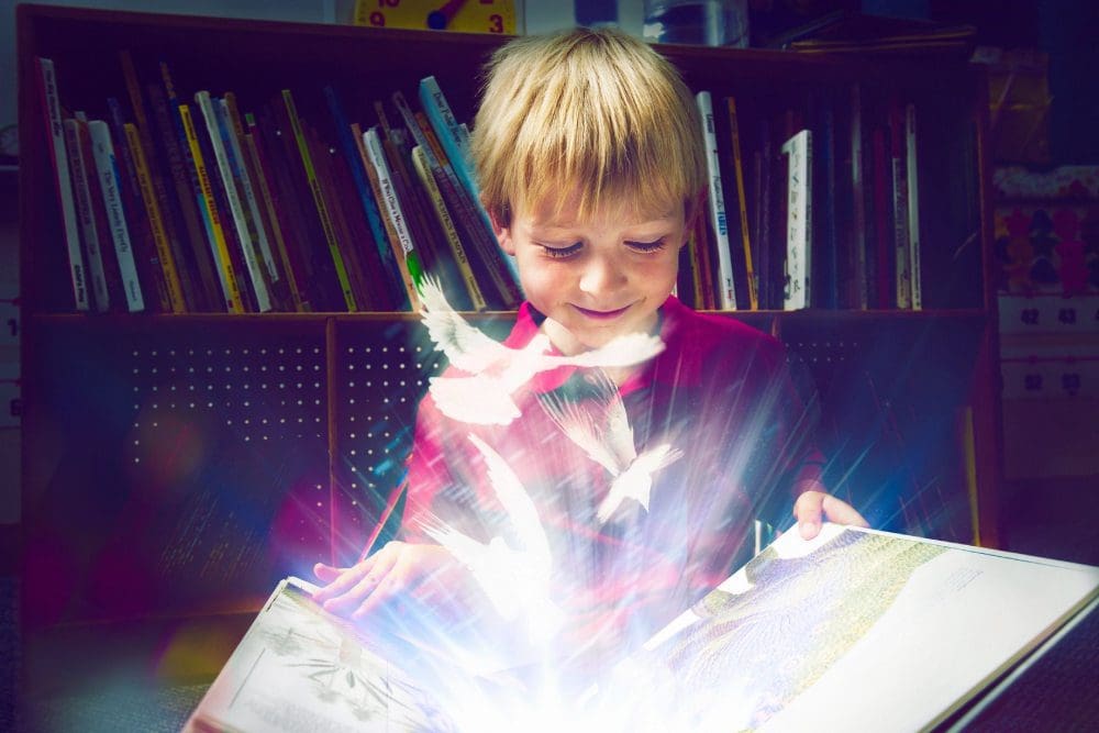 A young boy is reading a book with light coming from the bottom.